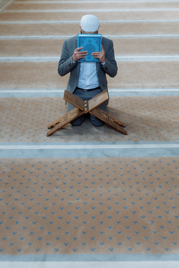 Man Holding a Koran Kneeling on the Floor of a Mosque